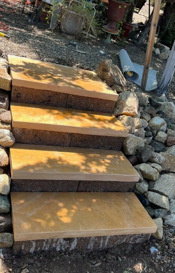 Sturdy stone steps leading up a hillside, surrounded by gravel and natural landscaping.