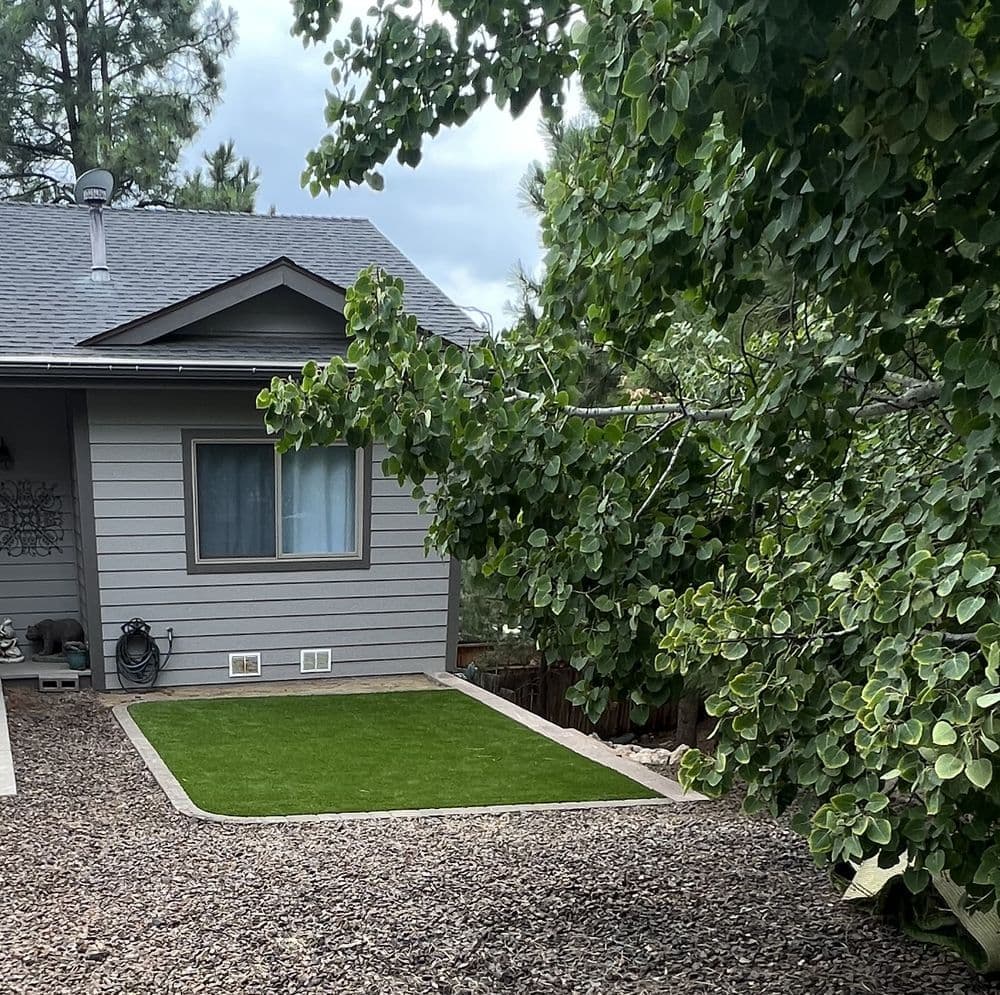 Home exterior with landscaped gravel yard and artificial grass area under a leafy tree.