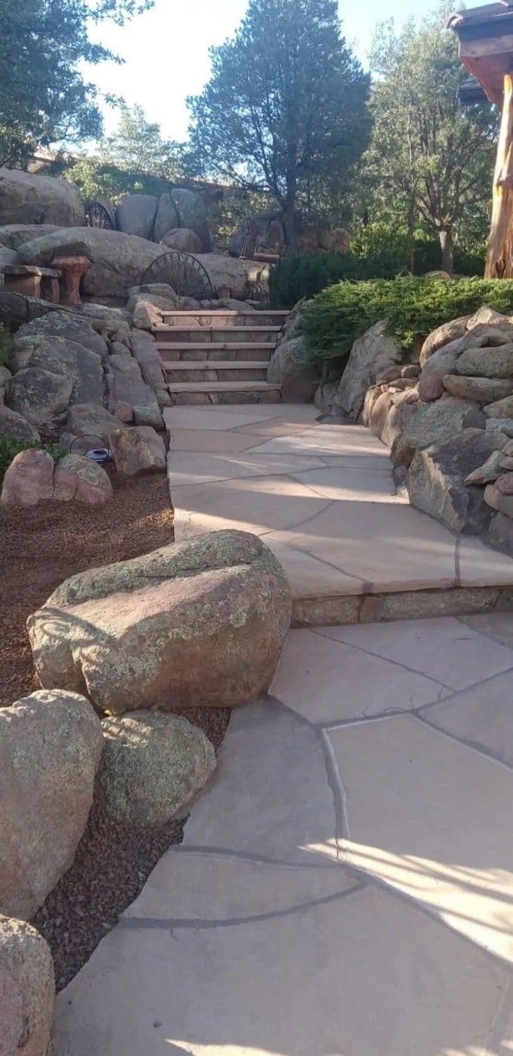 Natural stone pathway with steps, surrounded by rocks and greenery in a landscaped garden.