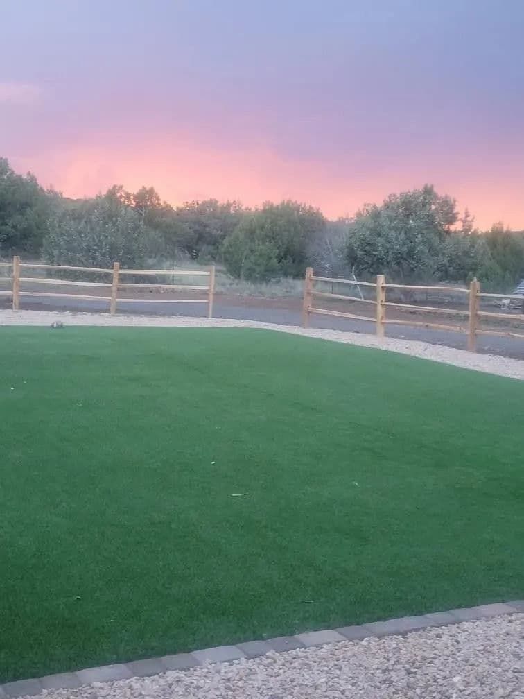 Lush green lawn with wooden fence and sunset sky in background.