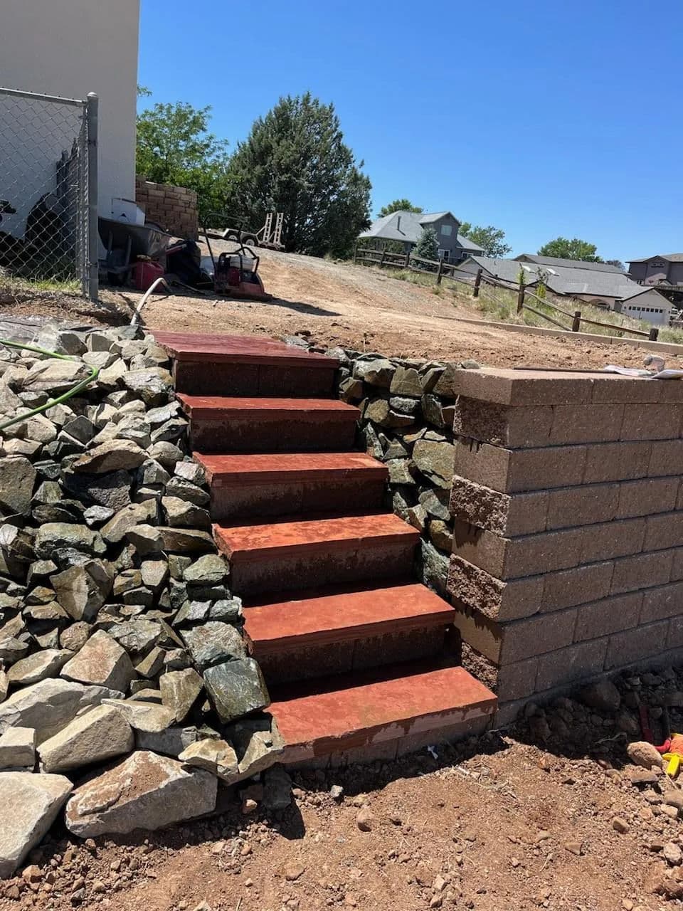 Red concrete stairs leading up to a house, surrounded by rocks and a stone wall.