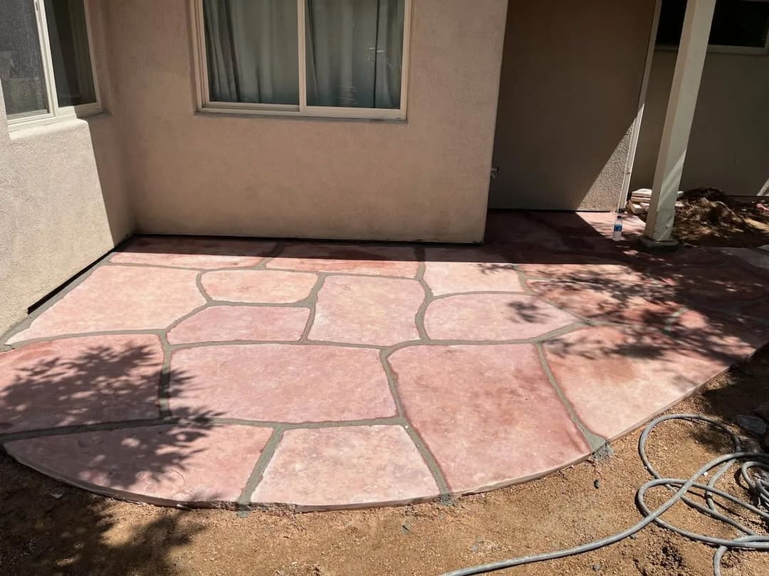 Decorative pink stone patio concrete installation with shadow from nearby bushes.