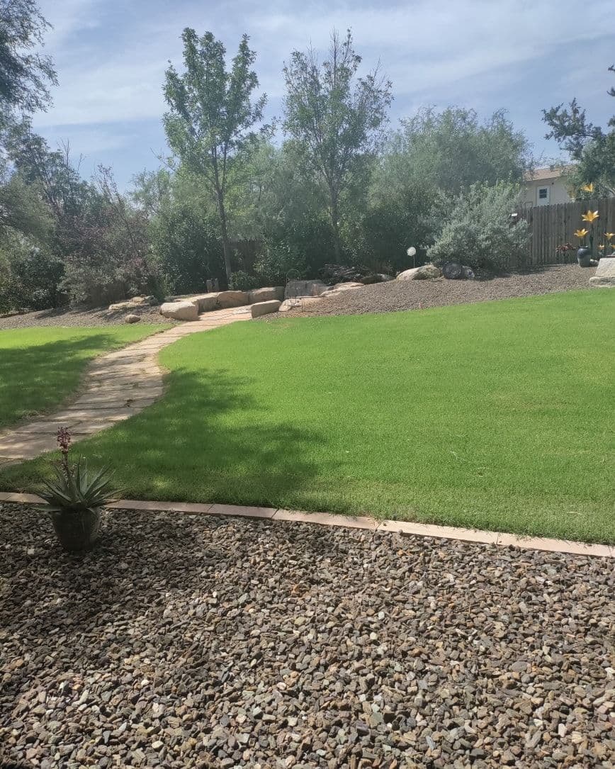 Lush green lawn with stone path and rocks in a serene backyard landscape.