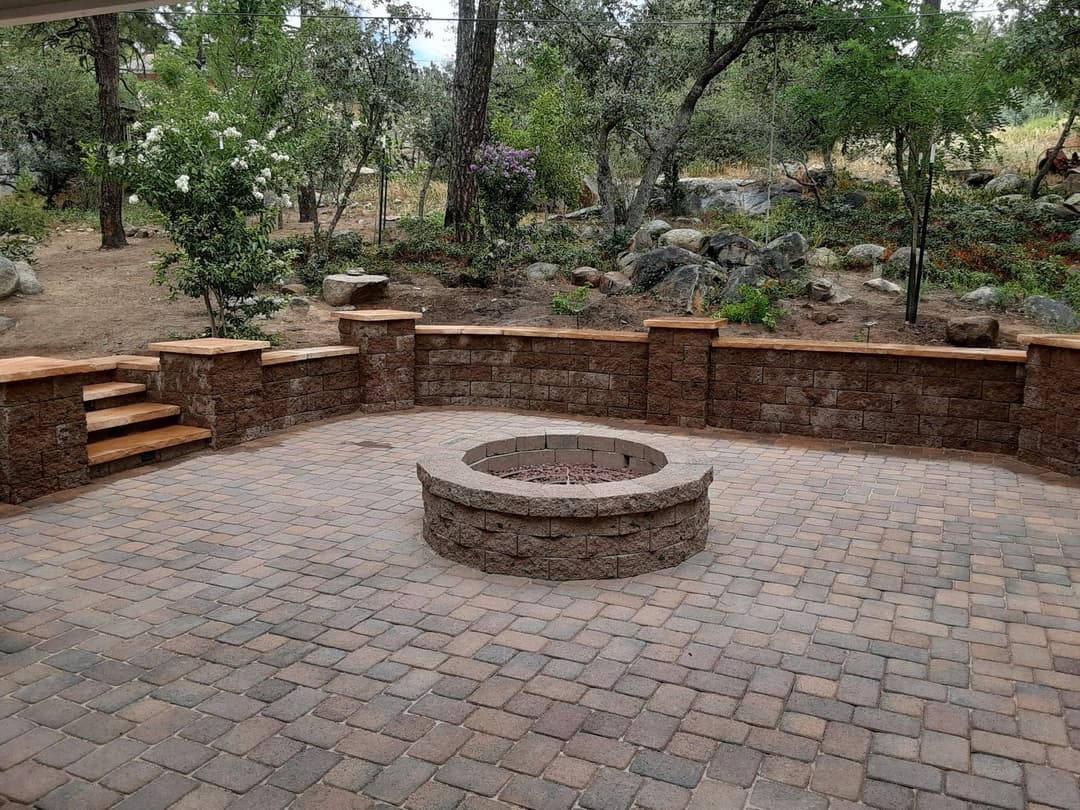 Outdoor patio with stone fire pit and natural landscaping featuring trees and boulders.