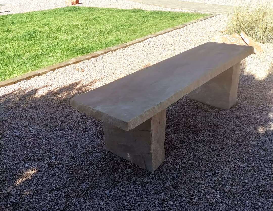 Stone bench on gravel with green grass in the background. Ideal for outdoor seating.