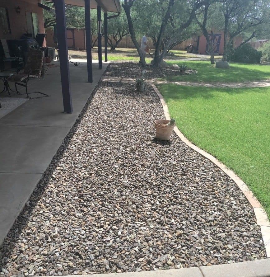 Gravel landscape design with stone path and potted plant in a sunlit backyard.