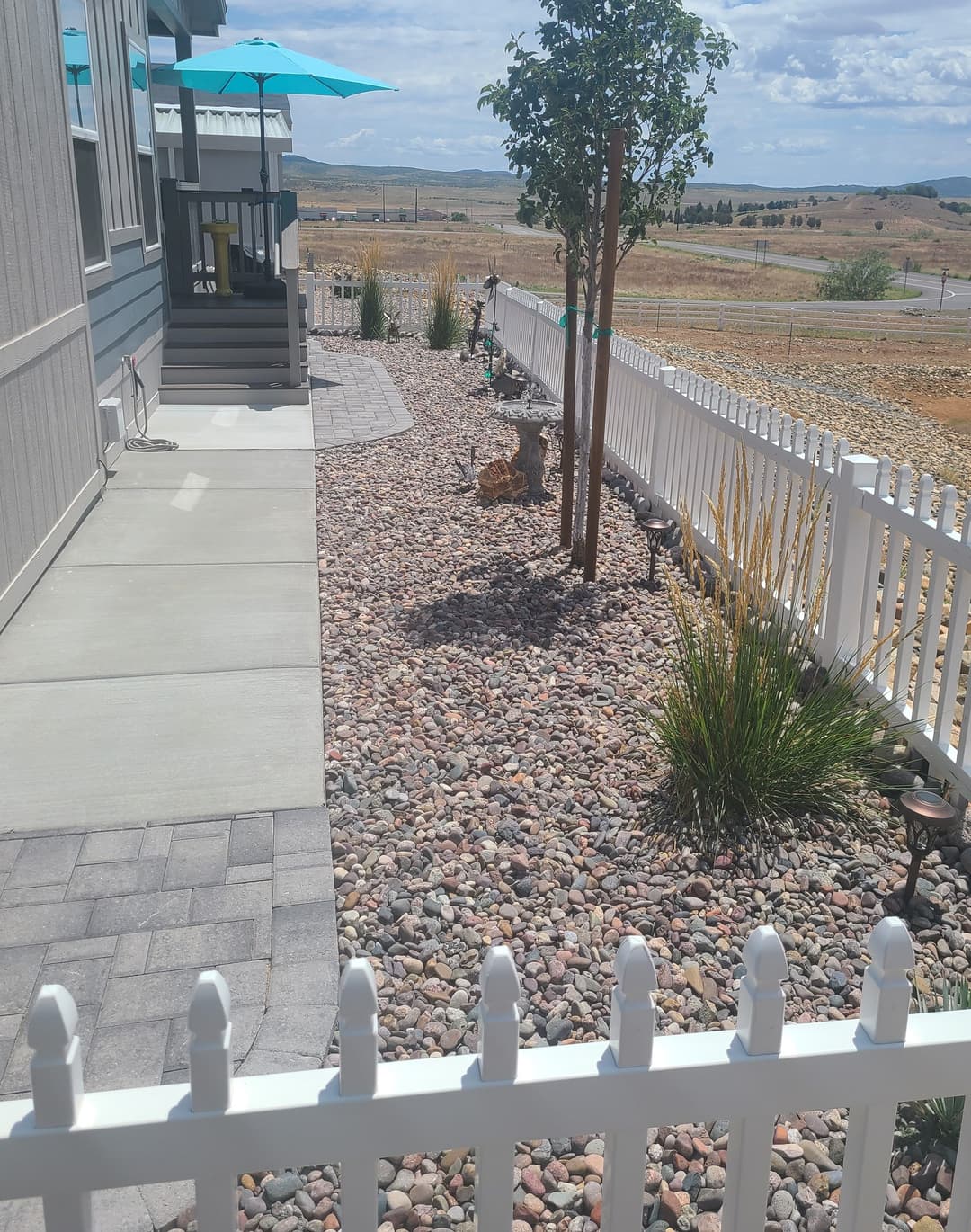 Landscaped yard with pebbles, plants, and a patio under an umbrella near a house.