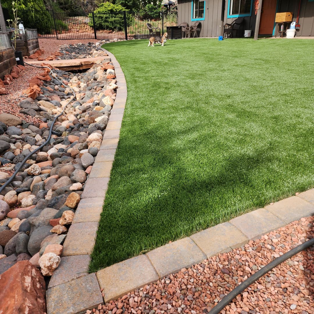 Lush green artificial grass lawn bordered by stone pathway and rocky landscape.