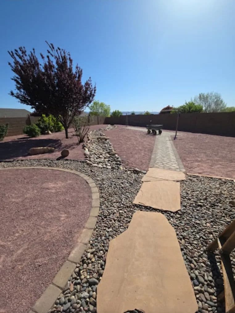 Landscape with rocky pathway and gravel yard under a clear blue sky.