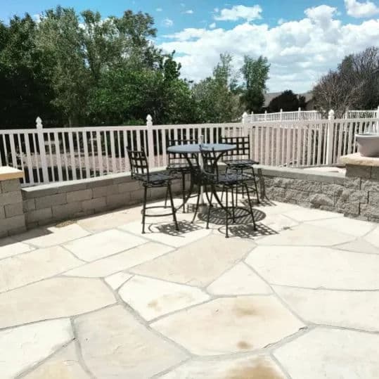 Outdoor patio with black metal furniture set against a scenic backdrop and white fence.