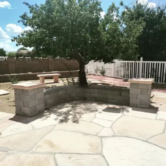 Outdoor patio with curved stone seating, a shade tree, and a white picket fence.